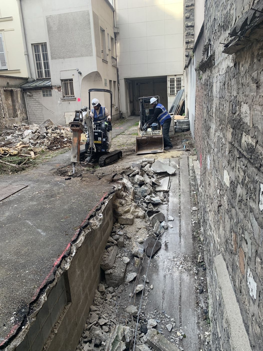 Compagnons MCE en tenue, mini-pelle en action dans une cour d'immeuble parisien
